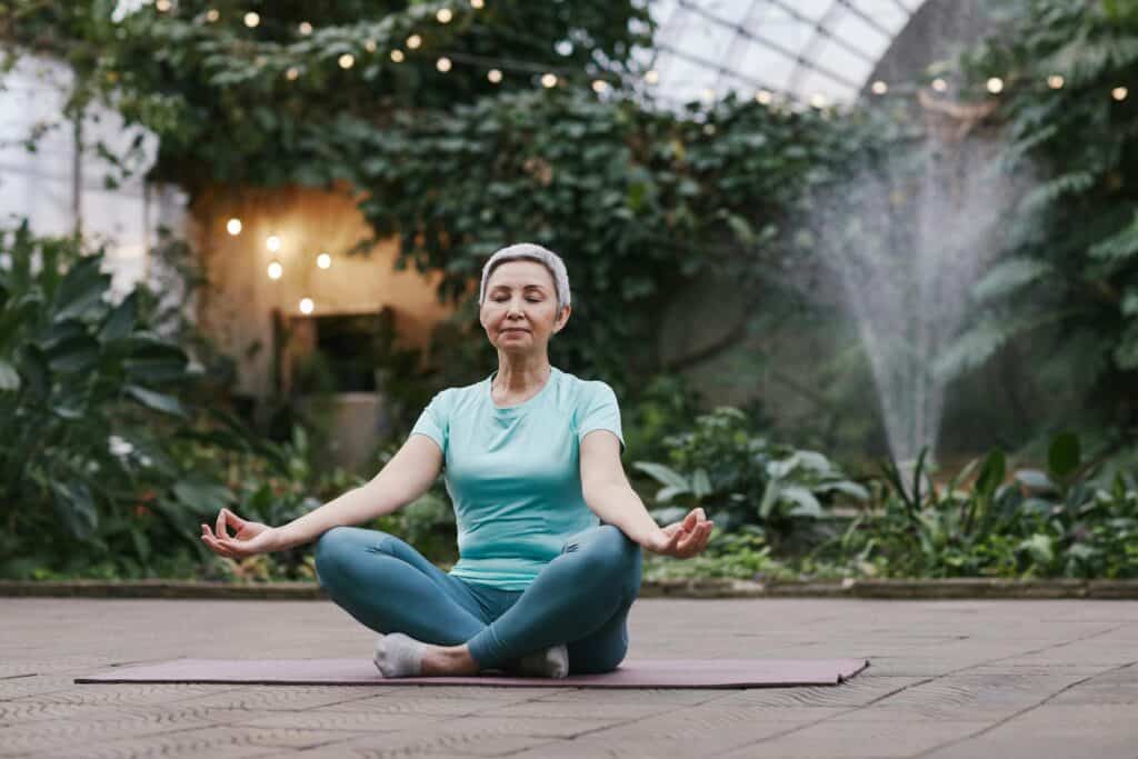 Elderly woman meditating in serene botanical garden setting, focused on wellness and mindfulness which helps in anxiety relief.